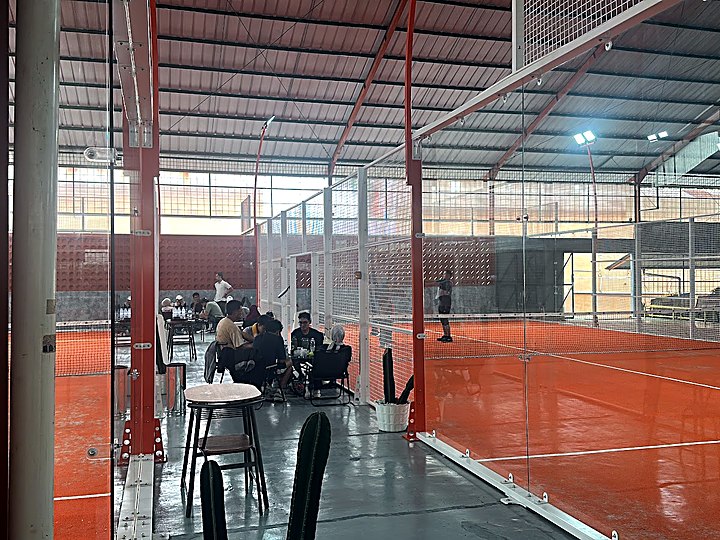 Court padel oranye di dalam gedung Disen Arena dengan area duduk penonton